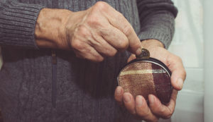 An elderly man puts a coin in an empty wallet.